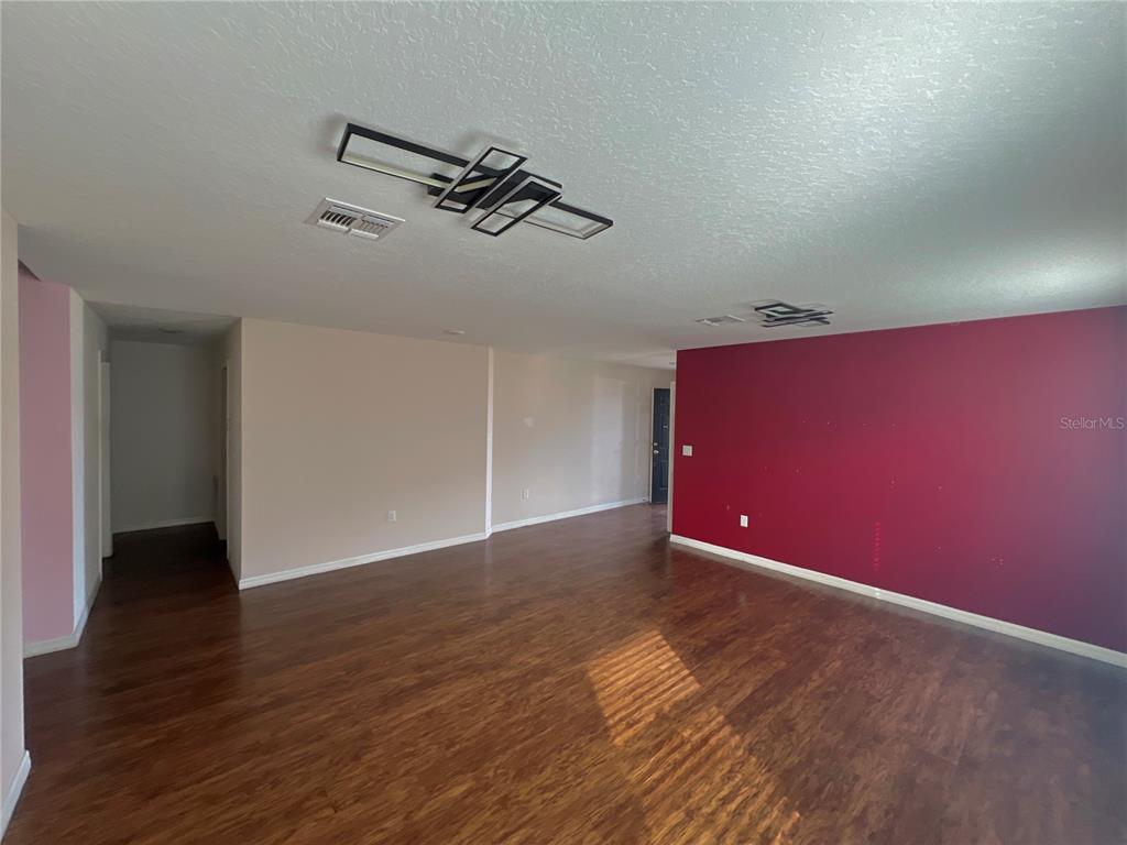 An empty room with dark wood-look flooring, beige walls, and one accent wall painted red — 205 BELLA VERANO WAY, DAVENPORT, FL
