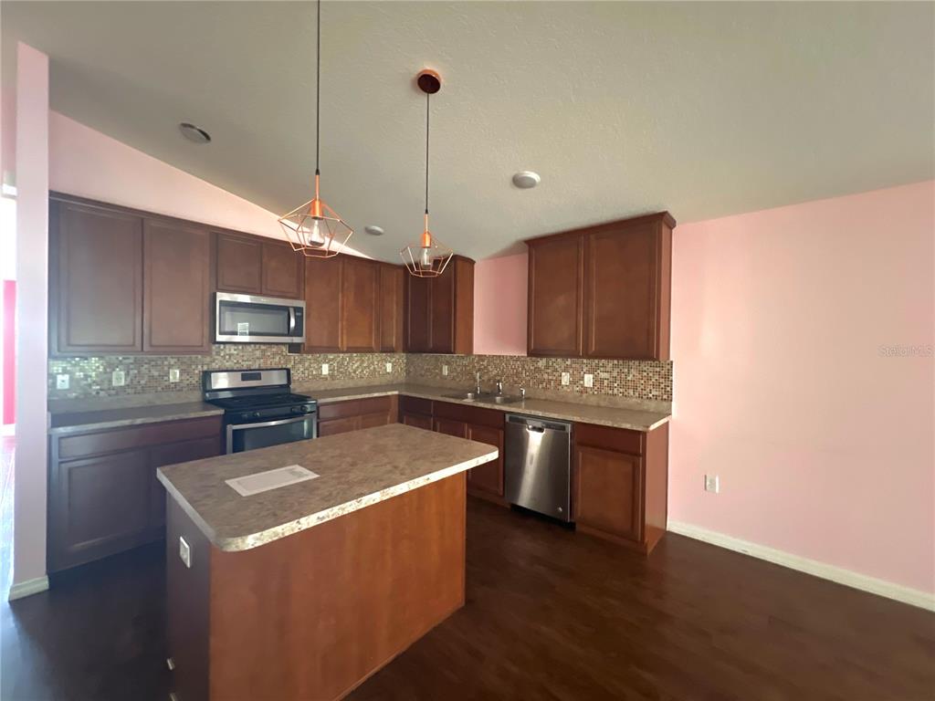 A kitchen features wood cabinets, a central island, stainless steel appliances, and pink walls — 205 BELLA VERANO WAY, DAVENPORT, FL