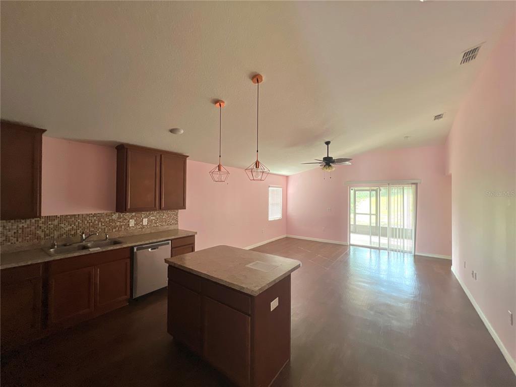 A kitchen with dark wood cabinets, a center island, and pink walls opens to a living area — 205 BELLA VERANO WAY, DAVENPORT, FL