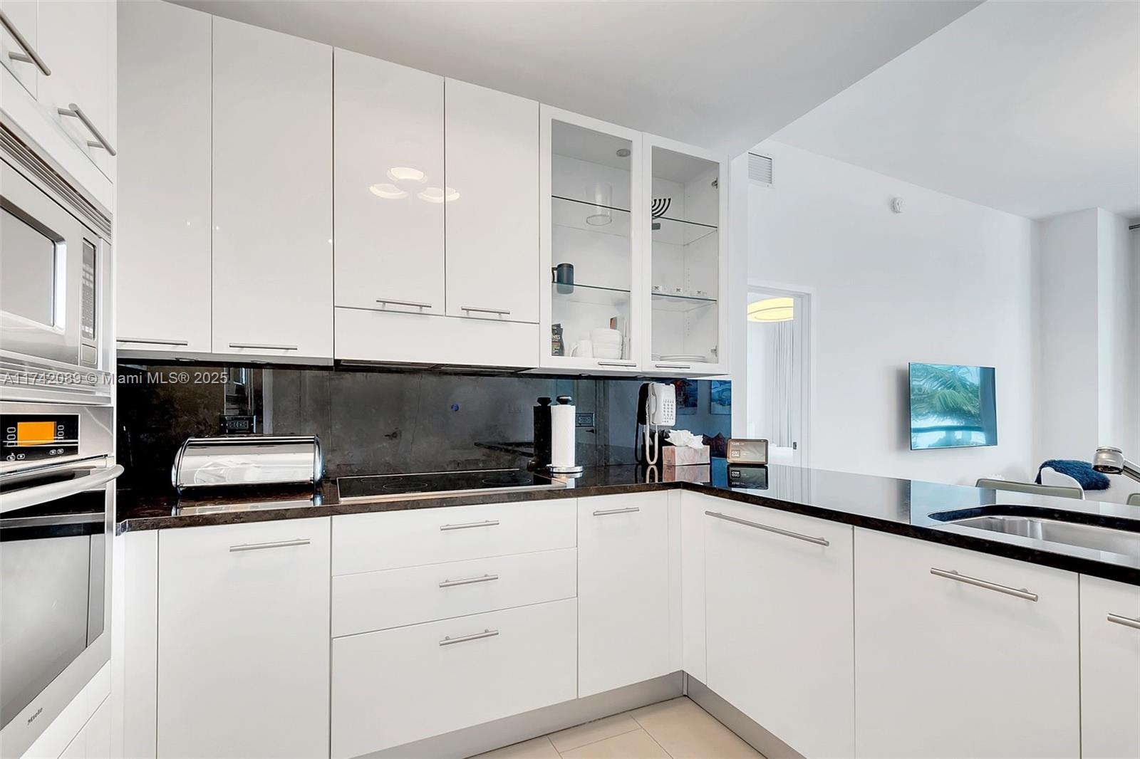 A modern kitchen features white cabinets, black countertops, and a dark stone backsplash — 6799 Collins Ave # 312, Miami Beach FL 33141, MIAMI BEACH, FL