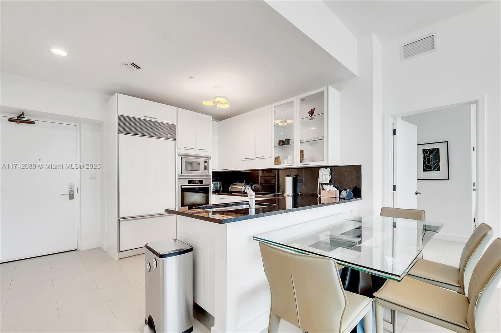 A modern kitchen features white cabinetry, black countertops, and a glass-topped dining table — 6799 Collins Ave # 312, Miami Beach FL 33141, MIAMI BEACH, FL