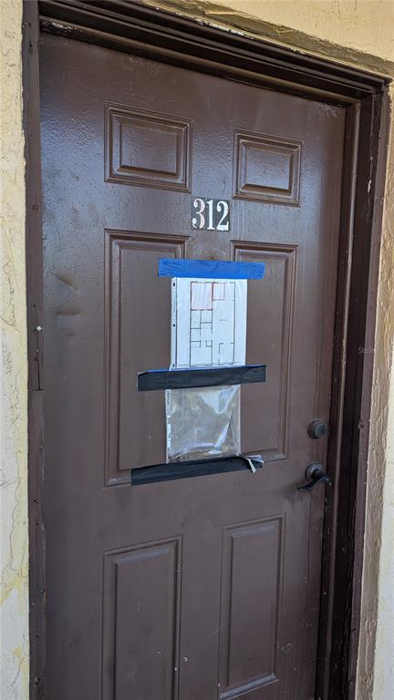 A brown apartment door labeled 312 has a floor plan taped to its center — 4087 LAKE BAYSHORE DRIVE UNIT 312, BRADENTON, FL