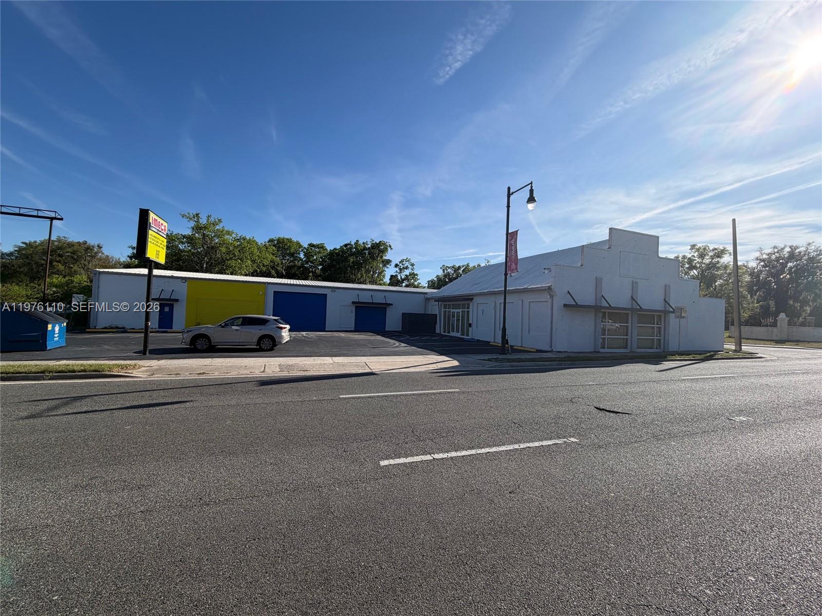 A commercial building with a parking lot and a blue dumpster sits along a road — 1201 E University Ave, Gainesville FL 32641, GAINESVILLE, FL