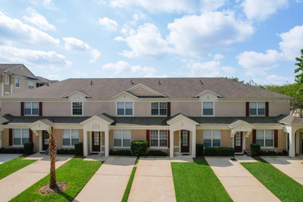 A row of multi-story townhomes with beige stucco siding, dark shutters, and individual concrete driveways — 8110 PRINCESS PALM LANE, KISSIMMEE, FL