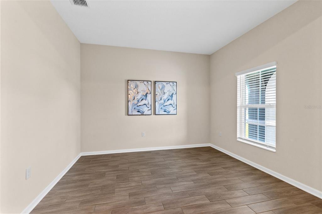 An empty room with light-colored walls, wood-look tile flooring, and two framed abstract artworks — 5311 AMERSHAM LANE, ST CLOUD, FL