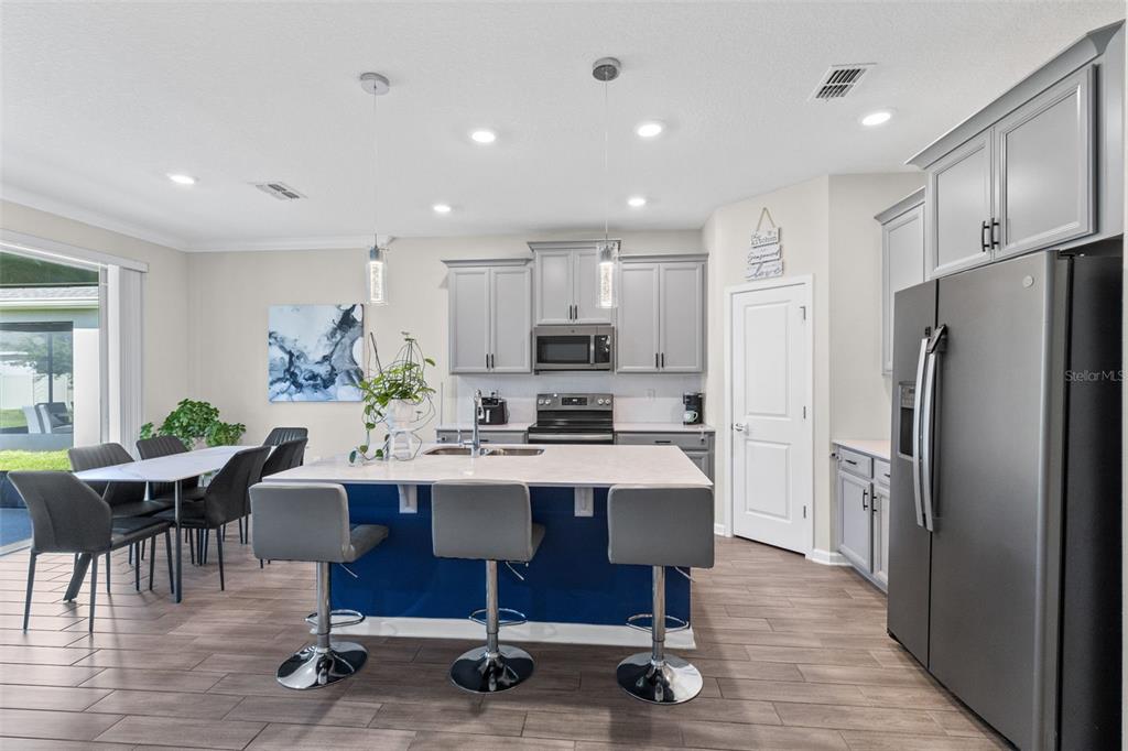 A modern kitchen features gray cabinets, a blue island with bar stools, and dining area — 5311 AMERSHAM LANE, ST CLOUD, FL