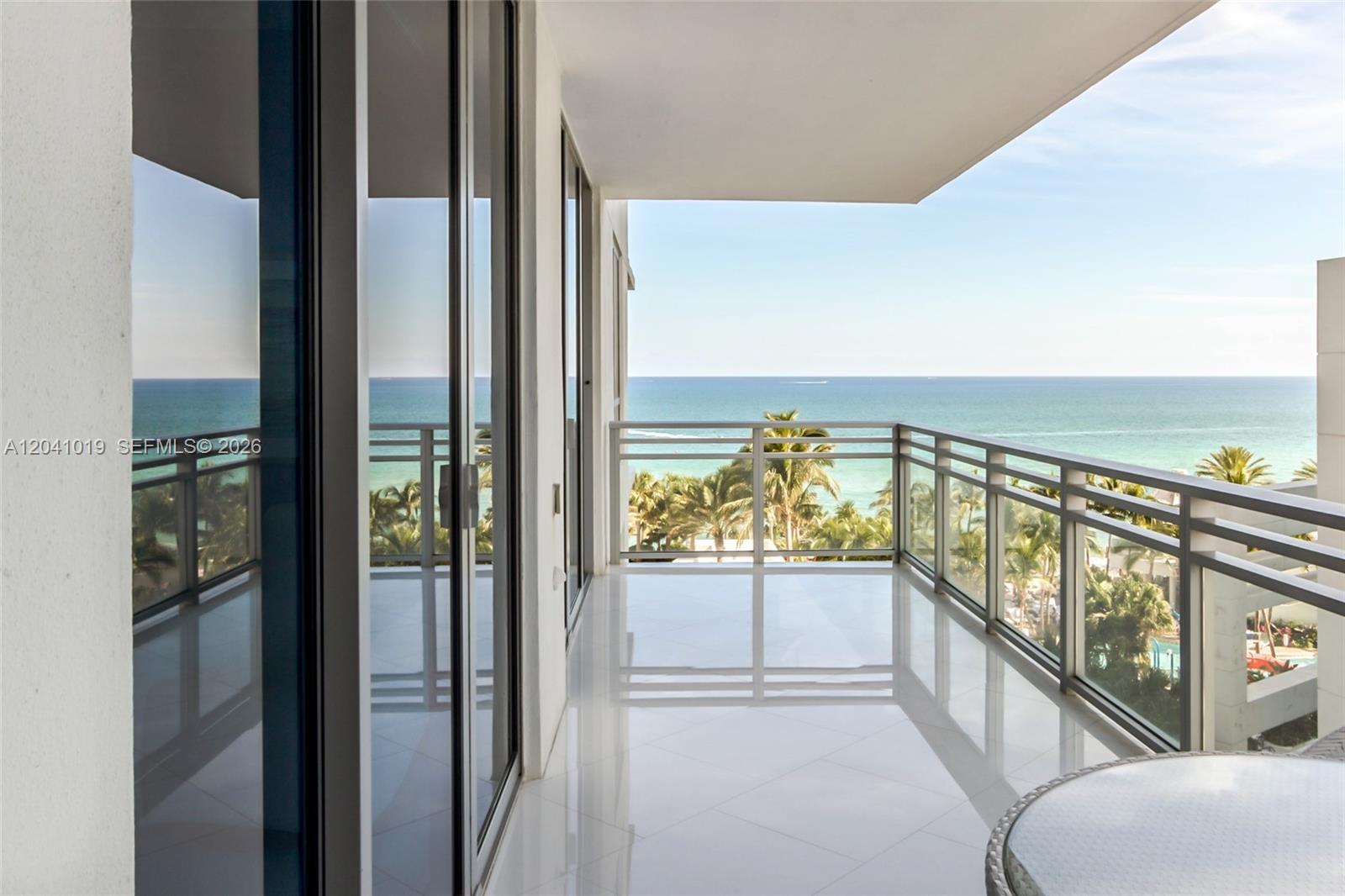 A balcony with white tile flooring and a glass railing overlooks the ocean and palms — 3535 S OCEAN DR # 705, Hollywood FL 33019, HOLLYWOOD, FL