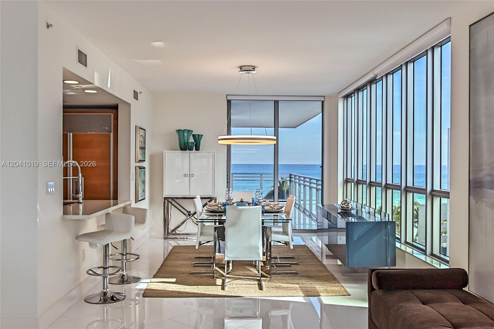 A dining area with a glass table, modern chairs, and floor-to-ceiling windows overlooking the ocean — 3535 S OCEAN DR # 705, Hollywood FL 33019, HOLLYWOOD, FL
