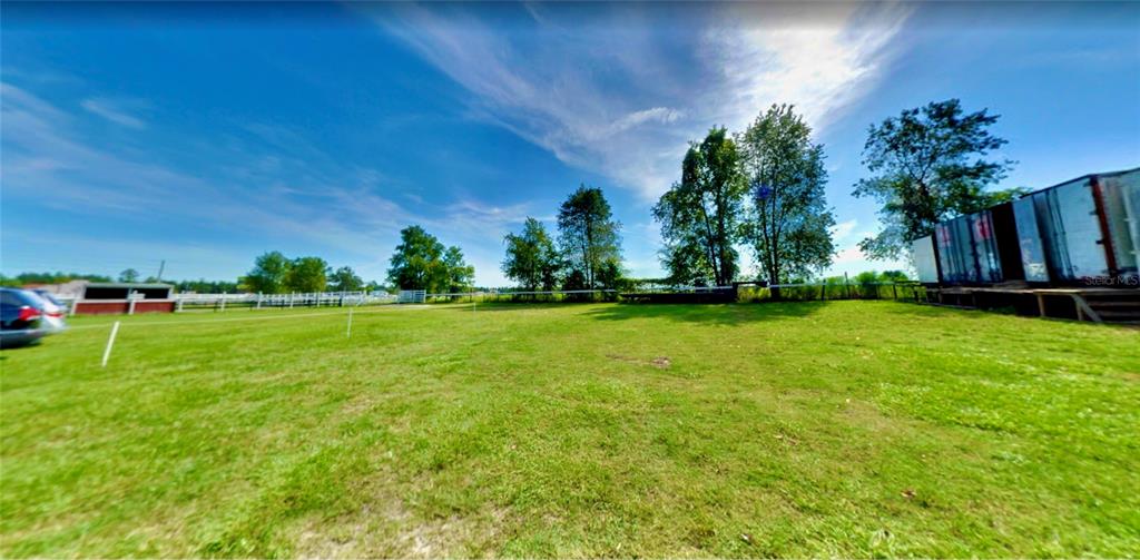 A grassy field features a white fence, scattered trees, and a large shipping container structure — 11150 W HIGHWAY 40, OCALA, FL