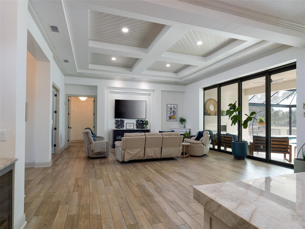 A living room features a coffered ceiling, wood-look tile flooring, and large sliding glass doors — 11920 SE 22ND AVE ROAD, OCALA, FL