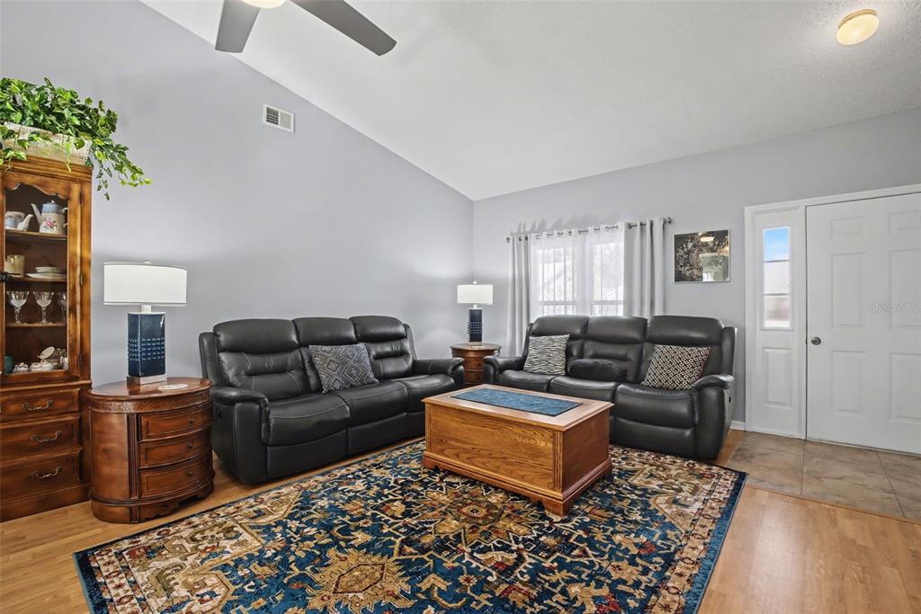 A living room features two black leather sofas, a wooden coffee table, and a rug — 25049 NAVEL AVENUE, LEESBURG, FL