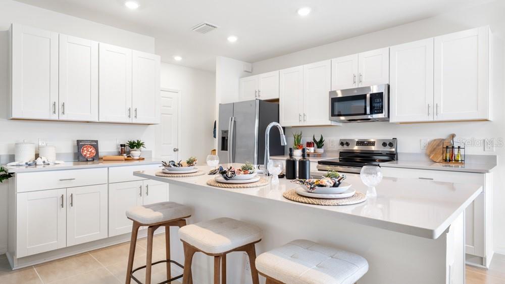 A modern kitchen features white cabinetry, stainless steel appliances, and a large quartz-topped island — 5422 CROWN POINT ROAD, KISSIMMEE, FL