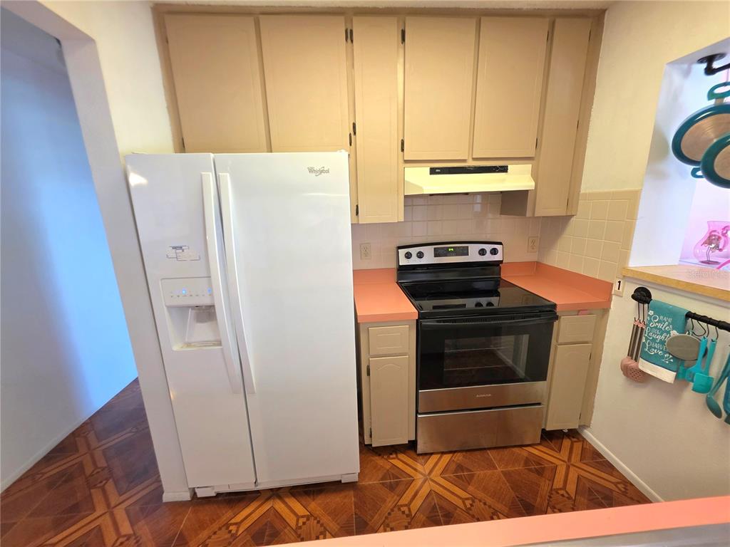 A kitchen features a white refrigerator, a stainless steel stove, and tan cabinets with pink countertops — 4164 GLADE ROAD, SPRING HILL, FL
