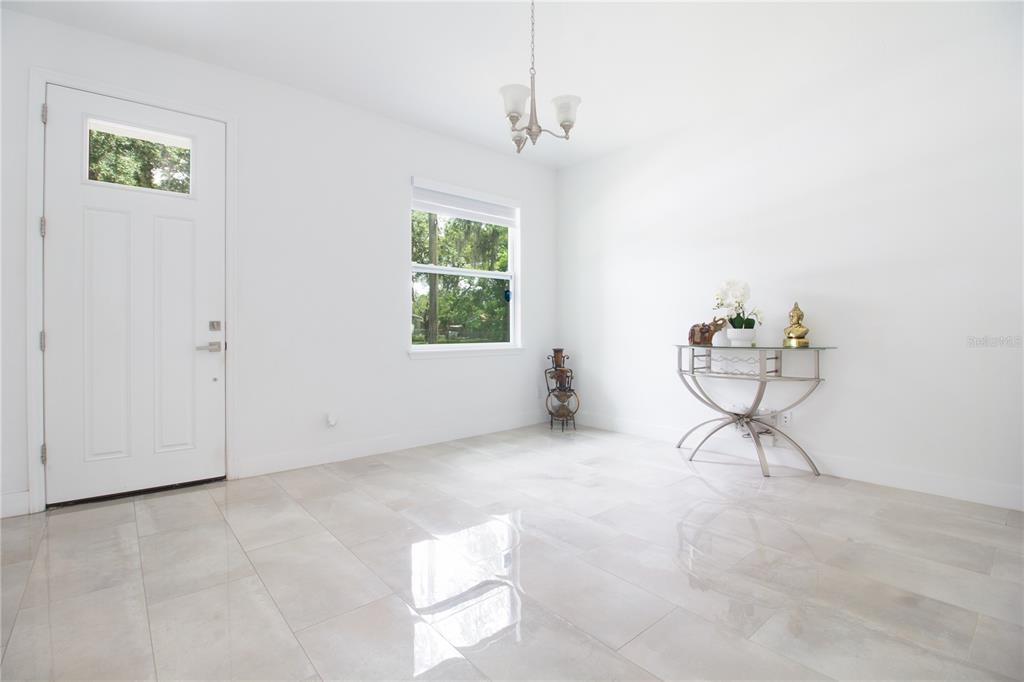 A bright room with white walls, large light-colored floor tiles, a window, and a chandelier — 8920 N NEWPORT AVENUE, TAMPA, FL