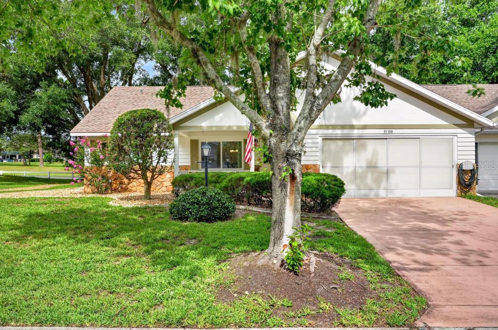 A single-story home features a stone facade, a white garage, and a large front tree — 9110 SW 89TH TERRACE UNIT A, OCALA, FL