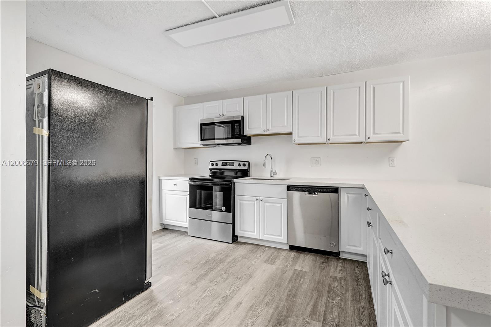 A kitchen features white cabinets, stainless steel appliances, a black refrigerator, and light wood flooring — 4800 Hillcrest Ln # 207, Hollywood FL 33021, HOLLYWOOD, FL
