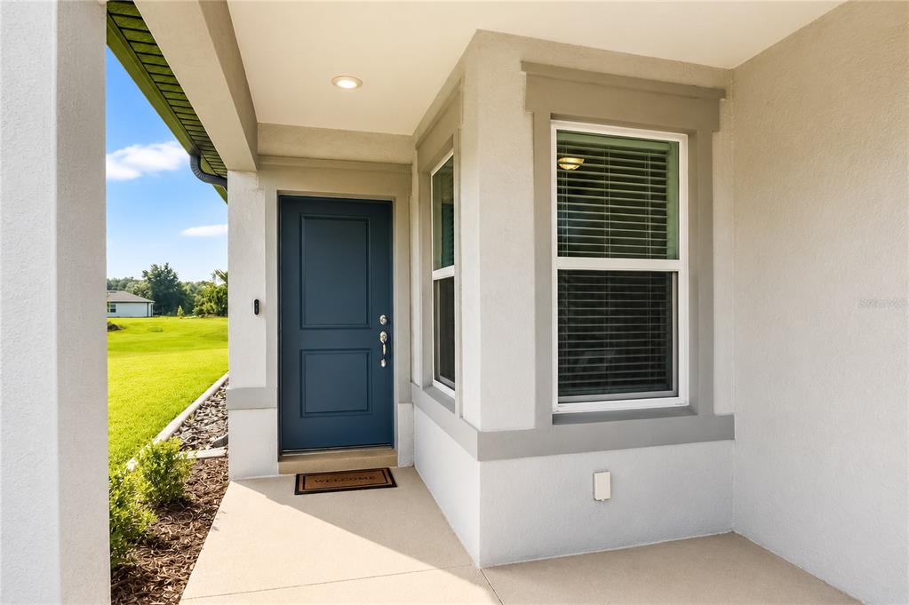 A covered entryway features a dark blue front door, a window, and a concrete porch — 5517 SW 85TH AVENUE ROAD, OCALA, FL