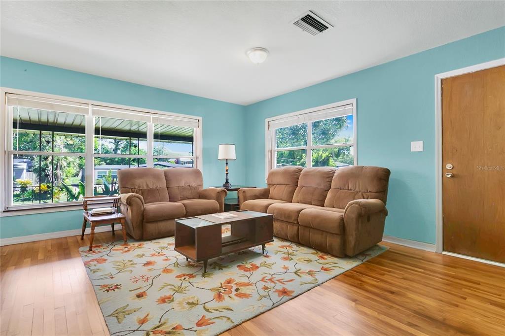 A living room features light blue walls, hardwood floors, a floral rug, and brown furniture — 2418 E JERSEY AVENUE, ORLANDO, FL
