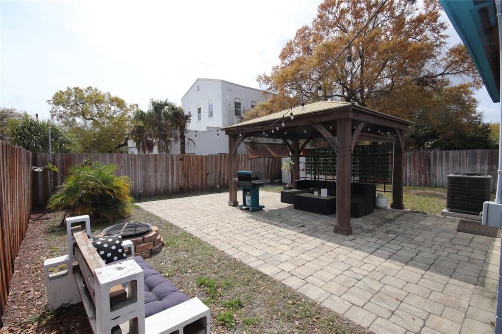 A backyard features a stone patio, a wooden gazebo, a grill, and a bench — 1918 W WALNUT STREET, TAMPA, FL