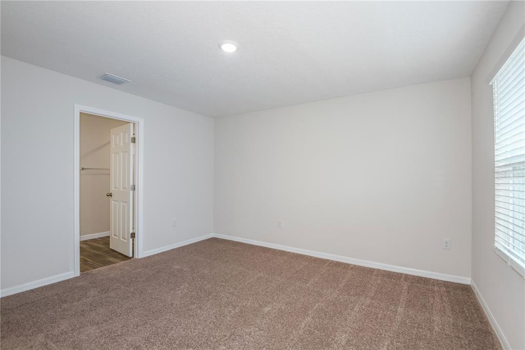 An empty bedroom features beige walls, brown carpet, a window with blinds, and a closet — 9892 PELICAN COAST DRIVE, DADE CITY, FL