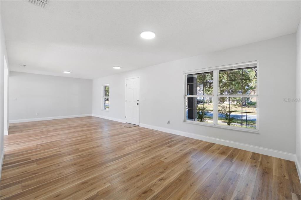 An empty room with light wood-look flooring, white walls, recessed lighting, and a front door — 1893 VALE DRIVE, CLERMONT, FL