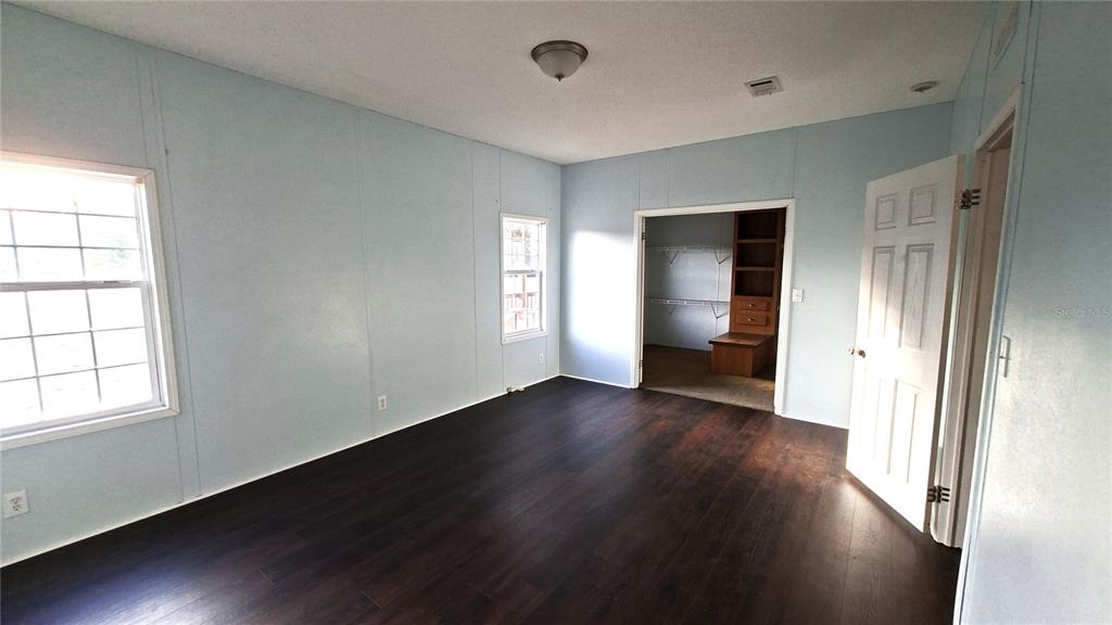 A bedroom with light blue walls, dark wood-look flooring, and an open walk-in closet — 3289 NE COUNTY ROAD 340, HIGH SPRINGS, FL