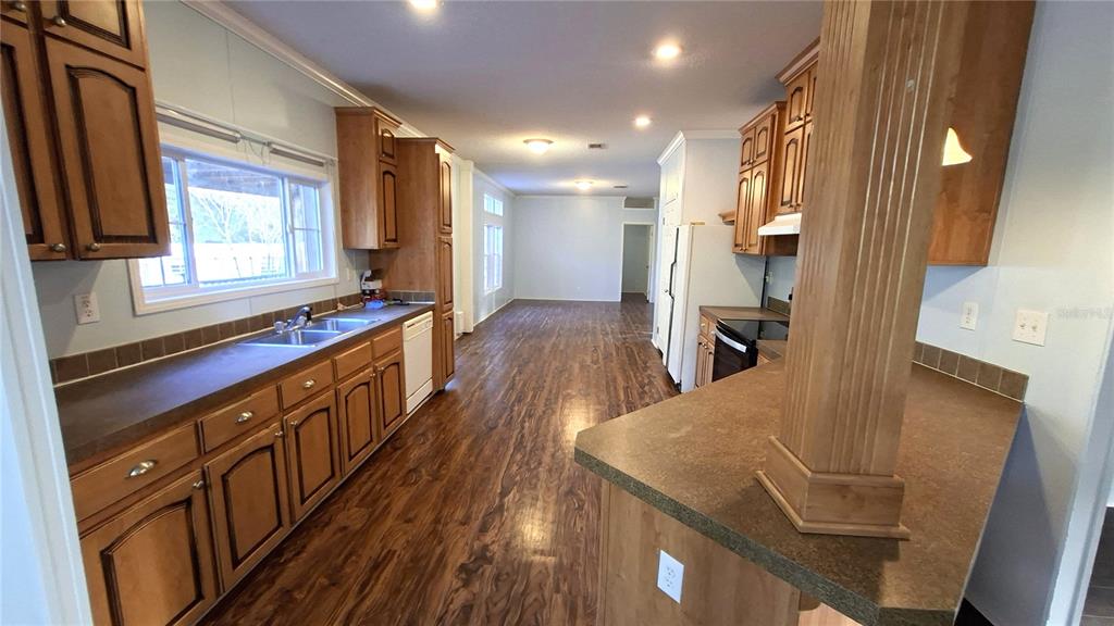 A kitchen with wood cabinets, dark countertops, and wood-look flooring opens into a living area — 3289 NE COUNTY ROAD 340, HIGH SPRINGS, FL