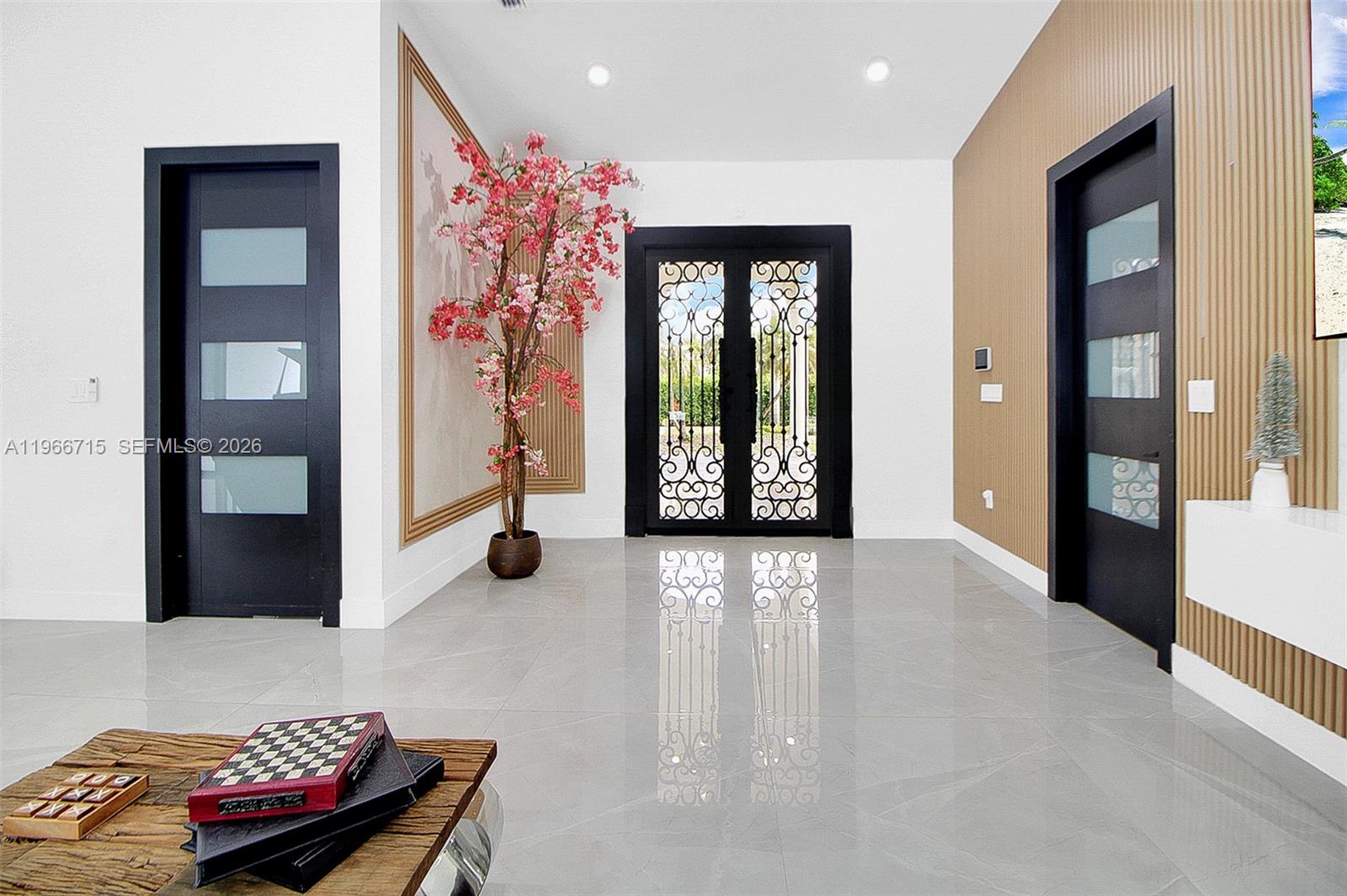 A modern entryway features a decorative iron double door, tiled floors, and wood-slatted wall accents — 2600 SW 128th Ave, Miami FL 33175, MIAMI, FL