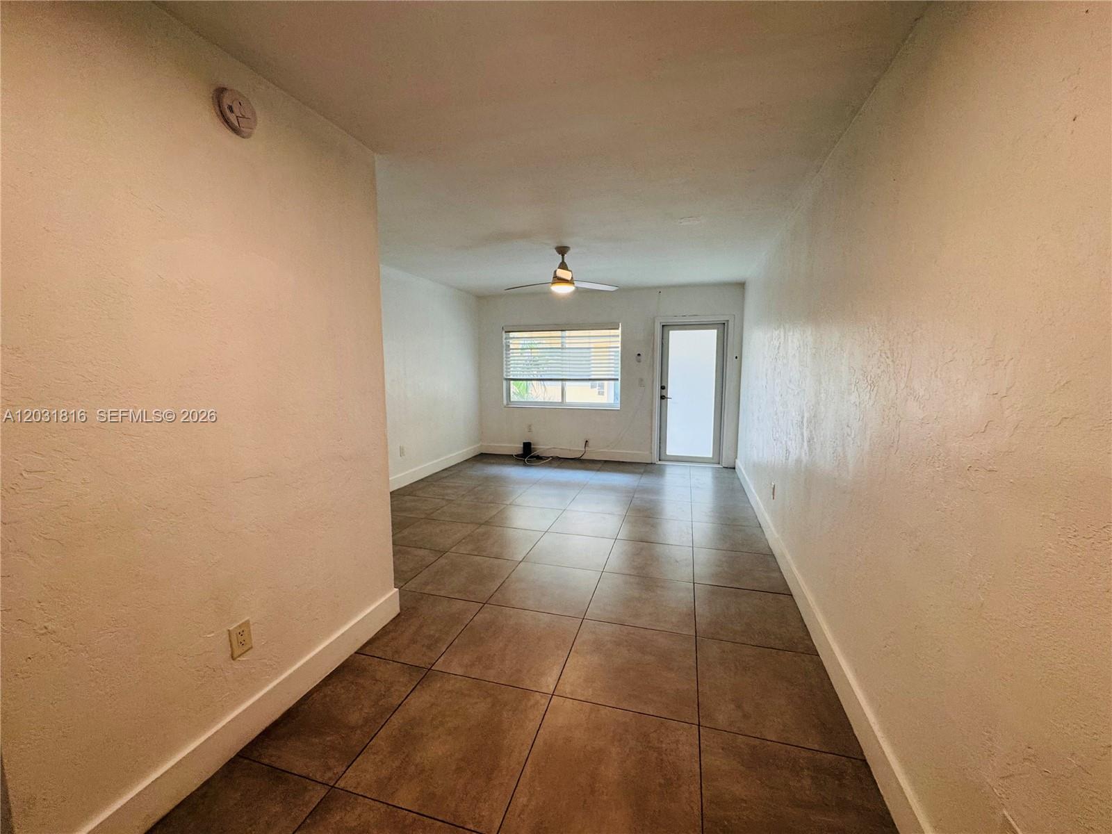 An empty room features white walls, large brown floor tiles, a ceiling fan, and a door — 75 Washington Ave # 10, Miami Beach FL 33139, MIAMI BEACH, FL