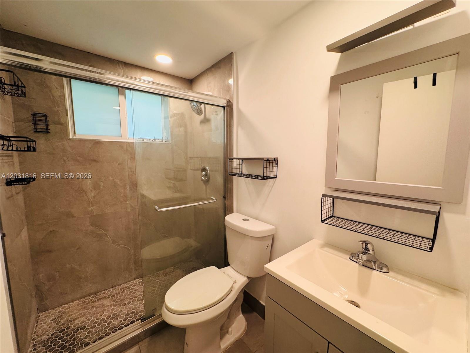 A bathroom features a glass-enclosed shower with stone tile, a toilet, and a vanity sink — 75 Washington Ave # 10, Miami Beach FL 33139, MIAMI BEACH, FL