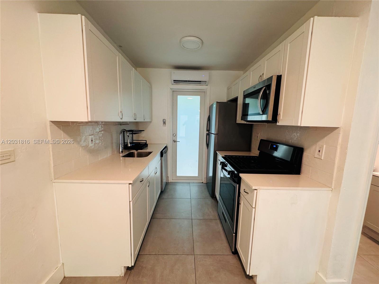 A galley kitchen features white cabinets, light countertops, stainless steel appliances, and tile flooring — 75 Washington Ave # 10, Miami Beach FL 33139, MIAMI BEACH, FL
