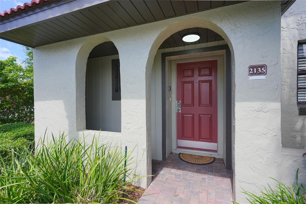 A red front door is set within a stucco archway featuring a brick walkway — 2135 WATER MANIA COURT, KISSIMMEE, FL