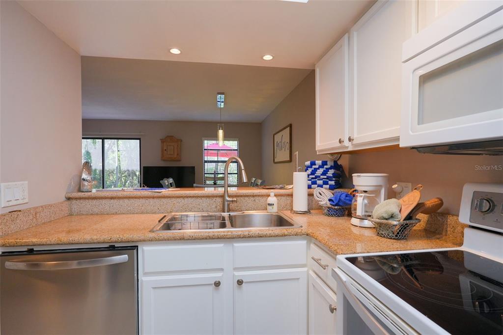 A kitchen features white cabinets, granite countertops, a stainless steel dishwasher, and a pass-through window — 2135 WATER MANIA COURT, KISSIMMEE, FL