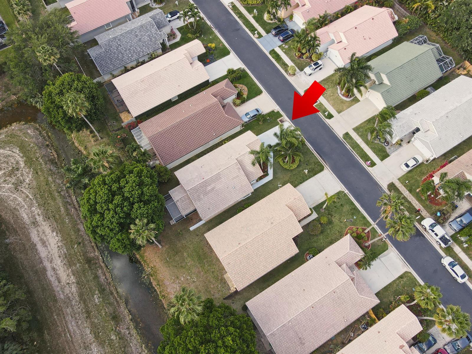 An aerial view shows a suburban street lined with houses, palm trees, and a canal — 1868 Barnstable Road, Wellington FL 33414, WELLINGTON, FL
