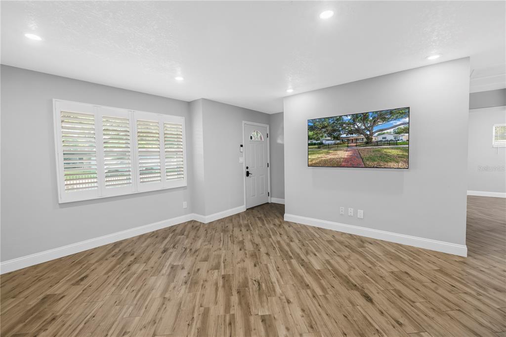 A bright living room features light gray walls, wood-look flooring, plantation shutters, and a wall-mounted television — 712 43RD AVENUE N, ST PETERSBURG, FL