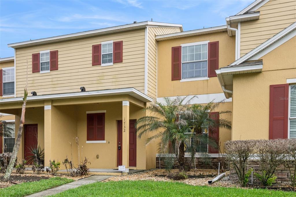 A two-story townhouse exterior with yellow siding, red shutters, and a covered front entryway — 1732 BUCKEYE FALLS WAY, ORLANDO, FL