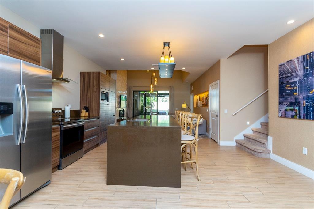 A modern kitchen features a large dark island, stainless steel appliances, and light wood-look flooring — 7505 BROOKLYN DRIVE, KISSIMMEE, FL
