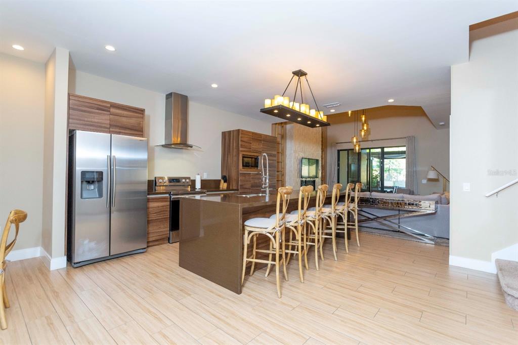 A modern kitchen features wood-grain cabinets, a large brown island, and a stainless steel refrigerator — 7505 BROOKLYN DRIVE, KISSIMMEE, FL