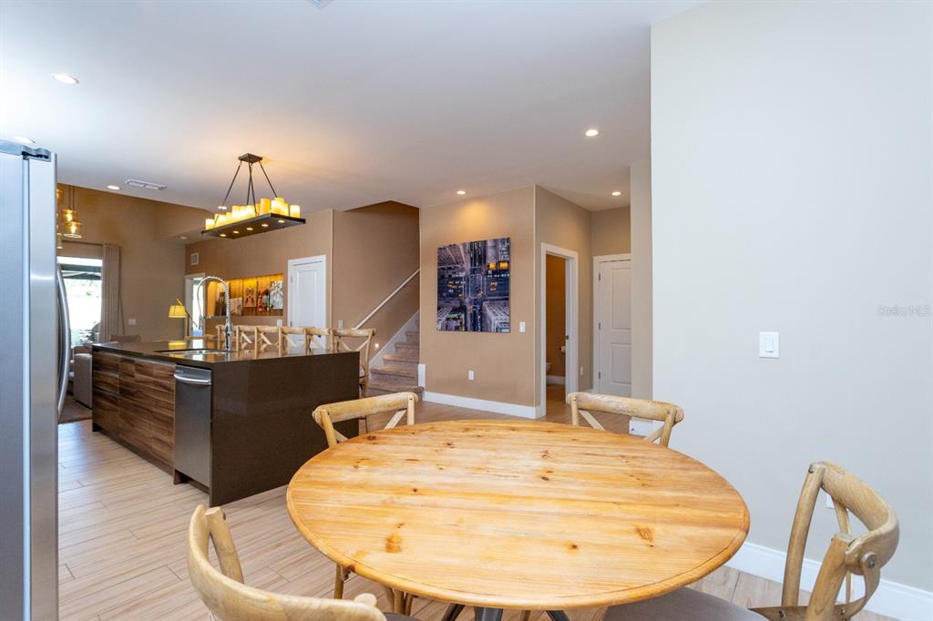A dining area with a round wooden table sits before an open kitchen and staircase — 7505 BROOKLYN DRIVE, KISSIMMEE, FL