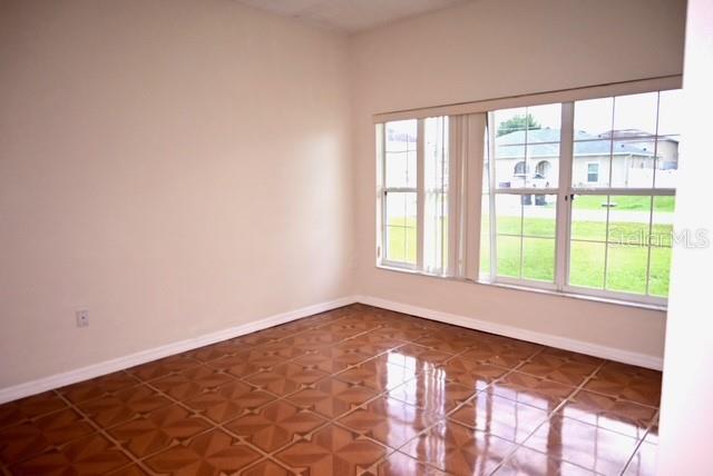 An empty room with tan walls, a glossy patterned tile floor, and large windows — 632 BITTERN COURT, KISSIMMEE, FL
