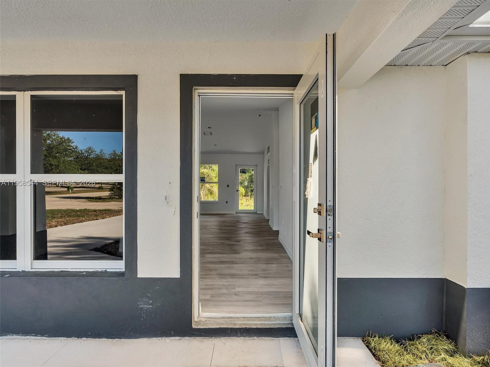 An open doorway reveals a bright interior with wood-look flooring and a rear exit door — 2401 E 11th St, Lehigh Acres FL 33936, LEHIGH ACRES, FL