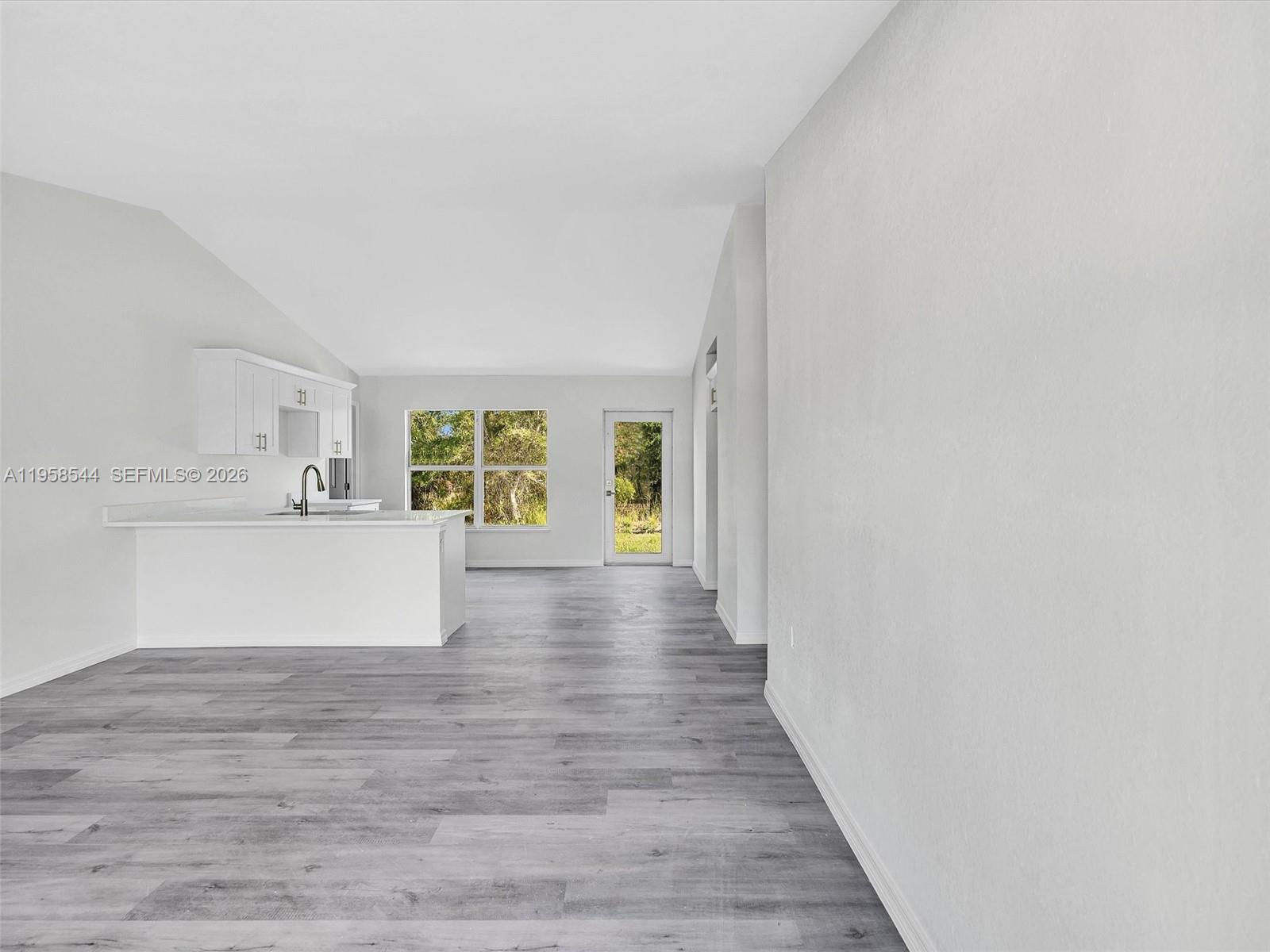 A kitchen with white cabinets and a peninsula overlooks an open living area — 2401 E 11th St, Lehigh Acres FL 33936, LEHIGH ACRES, FL