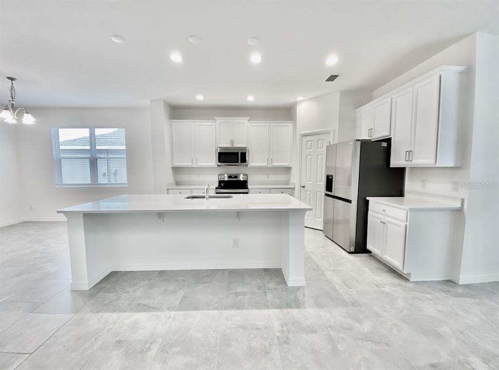 A modern kitchen features white cabinetry, a large central island, and stainless steel appliances — 924 AVENAL LANE, DAVENPORT, FL