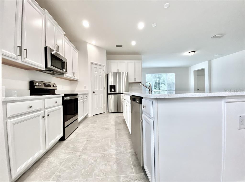 A modern kitchen features white cabinets, stainless steel appliances, and a large central island — 924 AVENAL LANE, DAVENPORT, FL