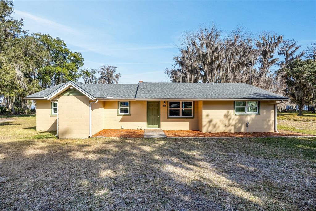 A single-story tan house with a green door sits on a grassy lot with trees — 16602 NE 124TH AVENUE, WALDO, FL
