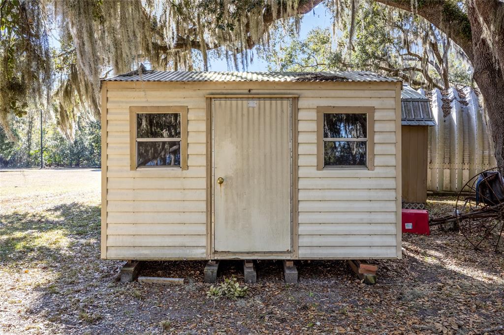 A small, light-colored shed with a corrugated metal roof sits on concrete blocks outdoors — 16602 NE 124TH AVENUE, WALDO, FL