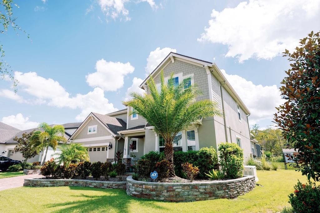 A two-story house with light-colored siding, a stone retaining wall, and a prominent palm tree — 8173 GAMEMASTER AVENUE, ORLANDO, FL