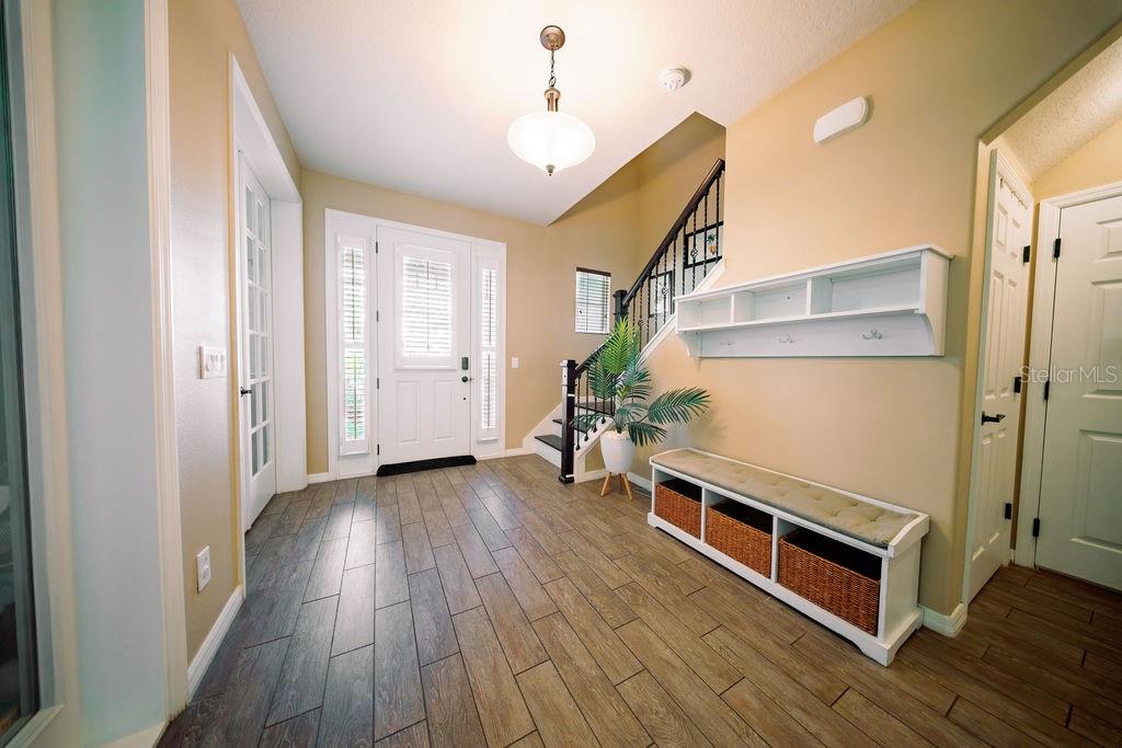 An entryway features wood-look tile flooring, a white front door, a staircase, and a bench — 8173 GAMEMASTER AVENUE, ORLANDO, FL