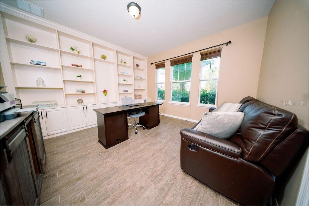 A home office features built-in white shelving, a dark wood desk, and a brown leather sofa — 8173 GAMEMASTER AVENUE, ORLANDO, FL