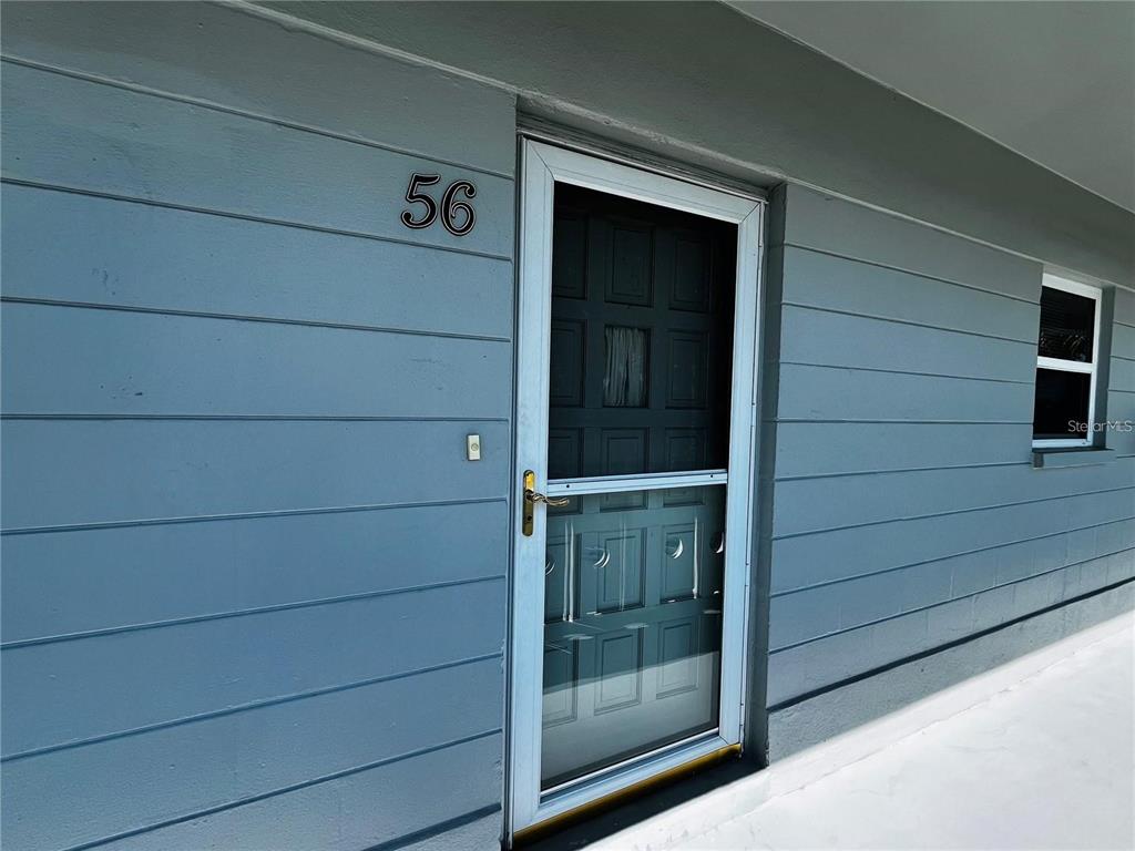 A blue-sided exterior wall features a front door with a screen and number 56 — 2340 GRECIAN WAY UNIT 56, CLEARWATER, FL